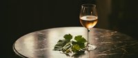 White wine glass with fresh grape leaves on marble table creating elegant dining atmosphere for restaurant menus and wine tasting events.