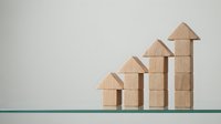 Wooden house blocks arranged in ascending growth pattern showing real estate market progression and property investment success on neutral background.