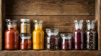 Colorful spices and seasonings in glass jars arranged on rustic wooden shelf. Kitchen organization and culinary ingredients for cooking and food preparation.