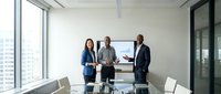 Diverse business professionals presenting financial data on digital display in modern conference room with city skyline views, suitable for corporate training and business communication materials.