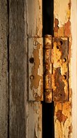 Weathered wooden door with rusty metal hinge showing peeling paint and aged texture. Vintage architectural detail with distressed surface for rustic design projects.