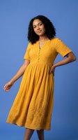 Young African American woman in yellow embroidered midi dress posing confidently against blue studio background for fashion and lifestyle content.