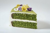 Green matcha cake slice with white cream layers and edible purple yellow pansy flowers on white background isolated for bakery menu design.