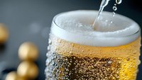 Fresh cold beer being poured into glass with bubbles and foam forming on top, extreme close up macro shot showing condensation and golden liquid.