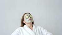 Young woman relaxing with cucumber eye mask in white bathrobe during spa treatment for skincare and wellness routine.