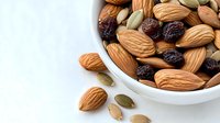 Fresh mix of raw almonds, pumpkin seeds and raisins in white ceramic bowl on light background, healthy snack for diet and nutrition.