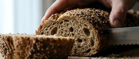 Whole grain bread sliced with knife, showing dense texture and seeds, hand holding loaf for baking and food photography.