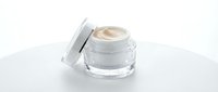 Cosmetic cream in clear glass jar with open lid on white surface, isolated for skincare product packaging and beauty design use.