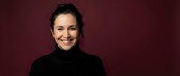 Smiling middle-aged Caucasian woman in black turtleneck sweater against burgundy background for professional headshot and business portrait photography.