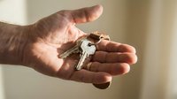 Male hand holding house keys with keychain in palm, real estate agent offering new home ownership, property purchase concept for buyers and renters.