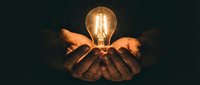 Hands cupping glowing vintage light bulb in darkness symbolizing creativity, innovation, inspiration and bright ideas for business concepts.