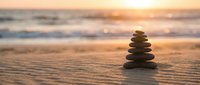 Zen stone stack on sandy beach at golden sunset with ocean waves creating peaceful meditation and mindfulness atmosphere for wellness and relaxation.