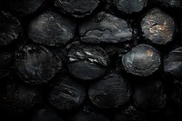 Dark charcoal briquettes with subtle golden highlights creating textural contrast, suitable for grilling, cooking, or industrial backgrounds.