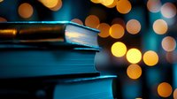 Stack of books against blurred golden bokeh lights creating magical atmosphere in dark blue tones, close up view with soft focus for reading and education concept.