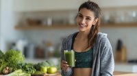 Young Caucasian woman in athletic wear holding green smoothie in modern kitchen, healthy lifestyle and nutrition concept for wellness content.