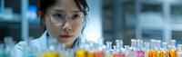 Young Asian female scientist in laboratory coat and protective glasses examining test tubes with colorful liquid samples for medical or chemical research.