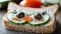 Creative sandwich with cat face made from cucumber slices, olives, and carrot on white bread, decorated with spices, fun food art for children's lunch.