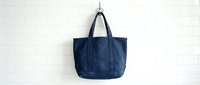 Navy blue canvas tote bag hanging on a hook against a white brick wall, casual everyday carry accessory for shopping or travel.