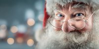 Close-up portrait of senior man with white beard, glasses and red hat smiling against blurred holiday lights background. Perfect for seasonal greeting cards.