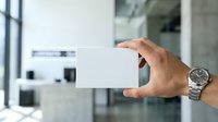 Man holding blank white business card in modern office environment with blurred background, suitable for corporate branding and professional identity design.