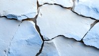 Cracked and peeling white paint on wall surface showing layers of deterioration and texture, creating abstract pattern of decay and weathered architectural detail.