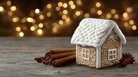 Festive gingerbread house with cinnamon sticks and star anise on wooden table against blurred golden bokeh lights background.
