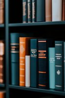 Vintage hardcover books arranged on wooden shelves in law library. Close-up view of classic bound volumes in blue, orange and teal colors creates scholarly atmosphere.