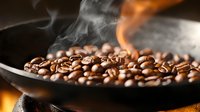 Fresh coffee beans roasting in black pan with rising smoke and flame, dramatic lighting captures aroma and artisanal coffee-making process in dark setting.