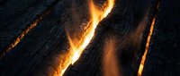 Dramatic volcanic lava flowing through dark rocky cracks creating intense orange glowing fissures with molten rock and fiery geological formations.