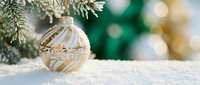 Elegant white and gold striped ornament resting on snow with evergreen branches and blurred festive lights in background, perfect for holiday and seasonal designs.