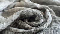 Soft linen fabric with natural wrinkles and folds in neutral gray tones creates organic texture and flowing curves, suitable for lifestyle and interior design projects.