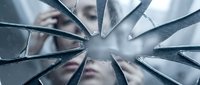 Shattered mirror fragments reflecting distorted face of young woman creating abstract broken glass pattern for psychological and mental health concepts.