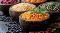 Raw colorful legumes and grains in wooden bowls on dark background. Fresh herbs garnish orange lentils, black beans, chickpeas and green peas. Food photography.