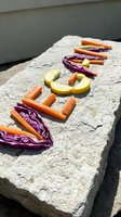 Word vegan spelled with fresh colorful vegetables on a stone surface outdoors, featuring carrots, red cabbage, and yellow squash in sunlight.