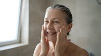 Senior woman with gray hair applying moisturizer to her face, skincare routine, anti-aging cosmetics, mature beauty and wellness concept for dermatology and cosmetic product marketing.