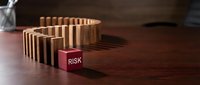 Wooden domino blocks lined up ready to fall with red risk block standing out from chain reaction concept for business failure prevention and crisis management.