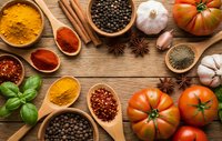 Colorful spices and fresh ingredients arranged on rustic wooden background. Turmeric, paprika, peppercorns, cinnamon, garlic, tomatoes and herbs for cooking.