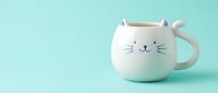Cute white cat-shaped ceramic mug with whiskers and ears on mint green background. Adorable kitty coffee cup for animal lovers and cozy morning routines.