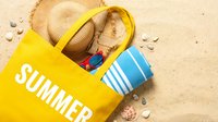 Yellow summer beach bag with straw hat, sunglasses, and striped towel on sandy shore, evoking vacation and travel vibes.