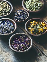 Assorted dried medicinal herbs and flowers in wooden bowls on rustic table. Natural healing ingredients include purple, yellow and blue petals for herbal tea and aromatherapy.