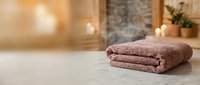 Folded mauve towel on marble counter in spa bathroom with candles and plants, suggesting relaxation and wellness for hospitality and home decor.
