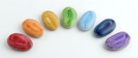Colorful gemstone collection arranged in a circle featuring polished oval stones in red, orange, yellow, green, blue, and purple hues, isolated on white background for design projects.