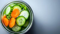 Fresh sliced cucumbers and carrots in glass jar with brine, top view. Homemade pickled vegetables for healthy eating and food preservation.