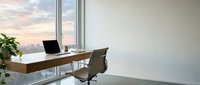Modern office workspace with wooden desk, laptop, and ergonomic chair positioned by floor-to-ceiling windows overlooking city skyline at sunset, featuring minimalist interior design for corporate environments.