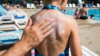 Adult applying sunscreen lotion to child's shoulder at poolside during summer vacation, sun protection and family care concept for beach and outdoor activities.