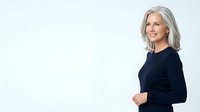 Mature woman with long gray hair, Caucasian ethnicity, wearing dark navy long-sleeve top, smiling confidently against white background. Suitable for business, healthcare, corporate portraits, and lifestyle marketing.