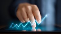 Businessman finger touching glowing blue financial chart graph on digital tablet screen showing growth trend and market analysis.