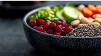 Fresh ingredients in black stone bowl with cranberries, chia seeds, nuts, cucumber and herbs. Healthy superfood concept for clean eating and nutrition.
