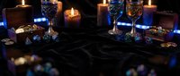 Elegant table setting with lit candles, crystal glasses, and scattered gemstones on dark marble surface for luxury event styling and upscale dining concepts.