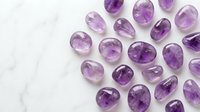 Collection of natural purple amethyst gemstones in various oval and round cuts scattered on white marble surface for jewelry making and design projects.